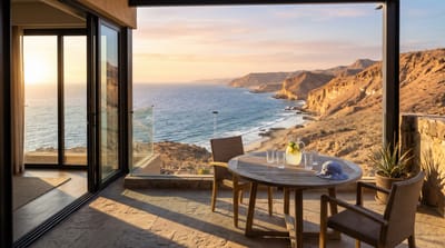 Balcony table with a pitcher of lemonade, four glasses and a child's sun hat overlooking sandstone cliffs and the sea at sunset