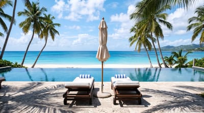 Two sun loungers and a closed umbrella beside an infinity pool overlooking a white sand beach, palm trees and turquoise sea